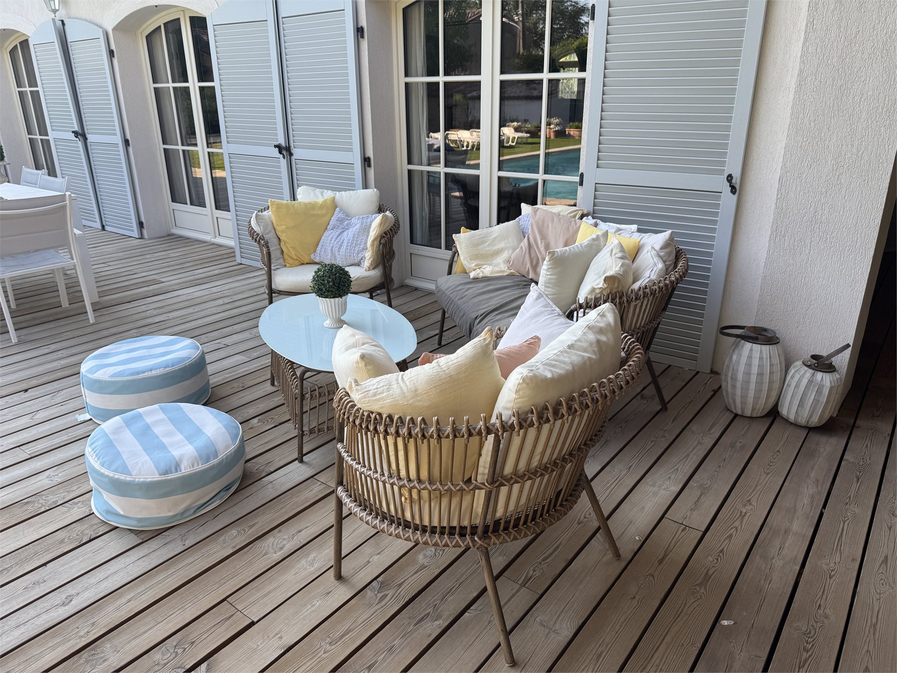 Le salon de jardin en rotin devant les volets de la maison